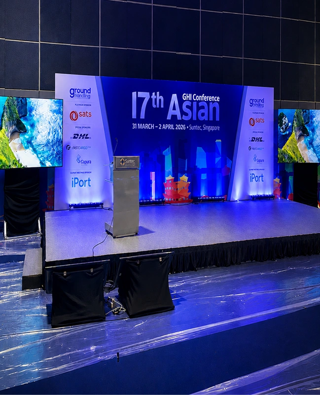 Conference stage setup at Suntec Singapore featuring podium, backdrop uplighting, and dual side TV display screens