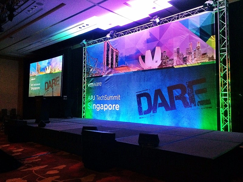 Corporate seminar stage with truss framework, branded backdrop banner, and side projection screen at Marina Bay Sands